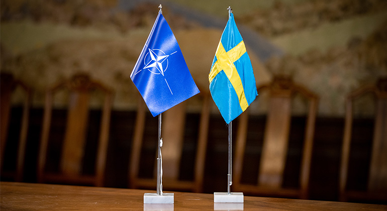 Natoflaggan och Sveriges flagga står sida vid sida på ett bord. 