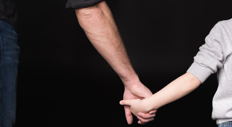 Närbild på en pappa och son som håller händer.
