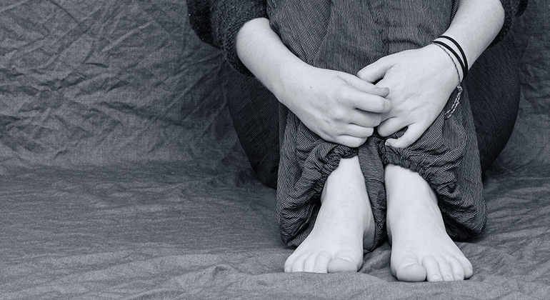 Bild på en person som sitter ihopkrupen med händerna runt benen. 