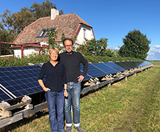 Ett par står framför ett hus med solcellspaneler på marken. Foto.