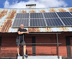 En man står på en ställning vid ett tak täckt med solceller. Foto.