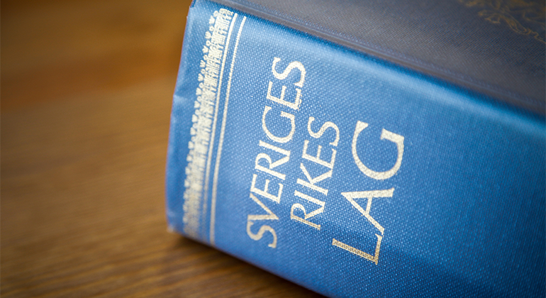 Blå bok med texten "Sveriges rikes lag" på ett träbord.