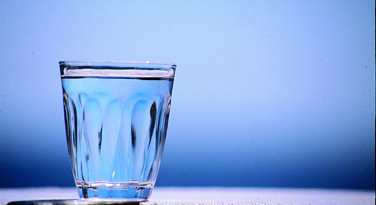Ett fyllt vattenglas mot blå bakgrund. 