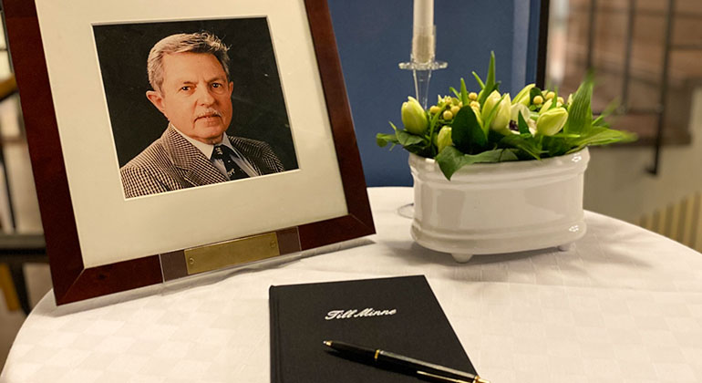 Foto på Sigvard Marjasin, kondoleansbok och ett ljus på ett bord i receptionen