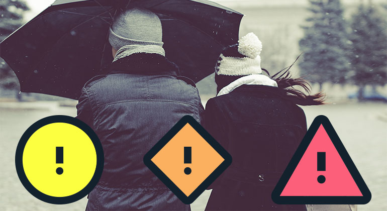 Två personer under ett paraply i snöoväder. På bilden syns också de nya varningssymbolerna för gul, orange och röd vädervarning som SMHI inför i april. 