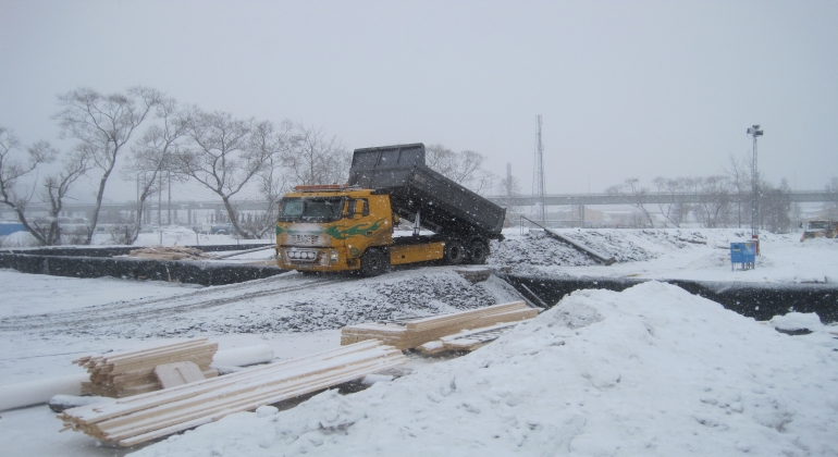 Lastbil tippar av sin last i ett snötäckt industriområde