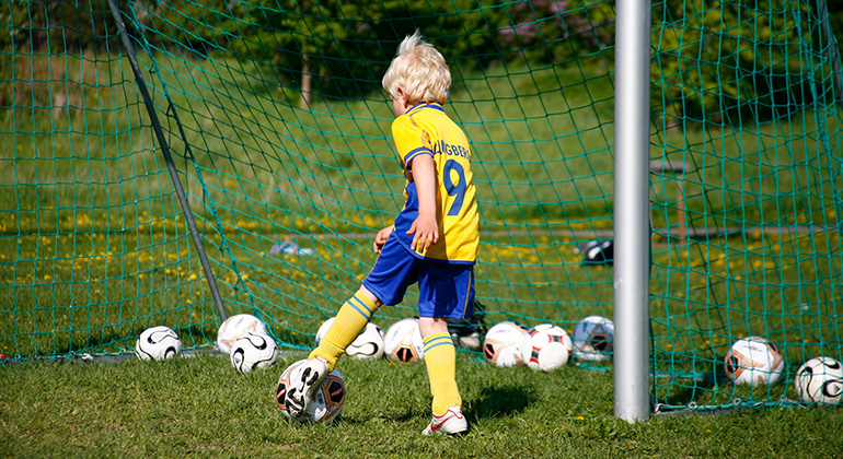 Barn som spelar fotboll i blågula fotbollskläder.