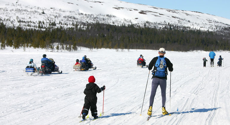Skoteråkare kör förbi familj som åker skidor.