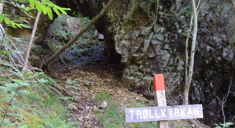 En skylt med texten Trollkyrkan framför öppningen i berget, som är som en gång.