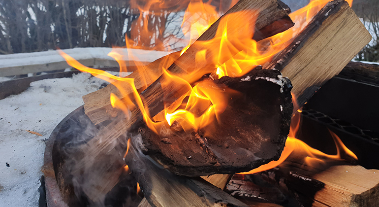 Närbild på ett vedträ som brinner i en brasa utomhus.