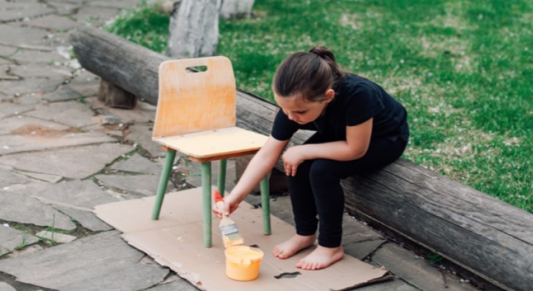 Bild på flicka som målar en stol med gul färg
