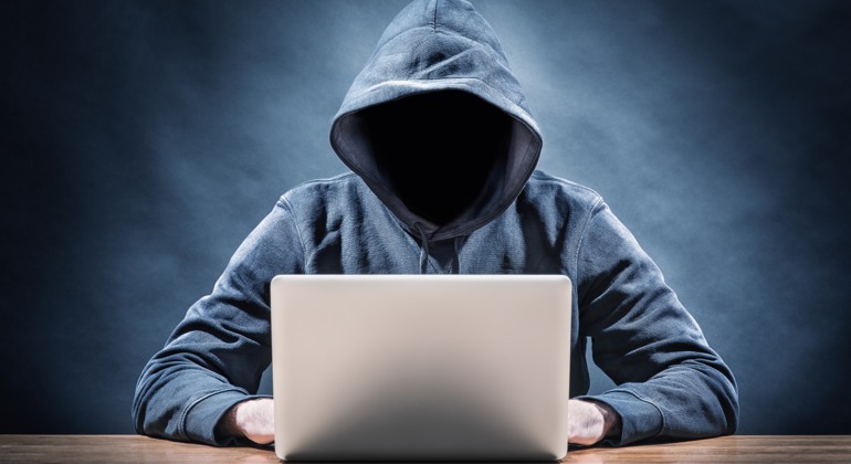 en person i hoodie sitter framför en laptop