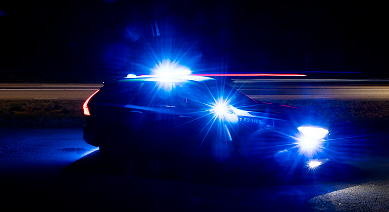 Bild som visar en polisbil i mörker. Bilen har påslaget blåljus
