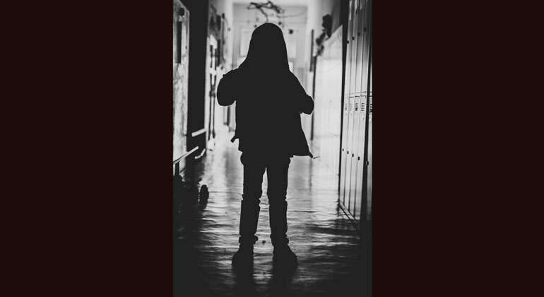 Siluetten av ett barn som står i en mörk korridor.