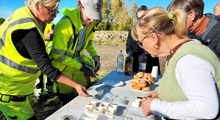 Arkeologer och representanter från Länsstyrelsen, bland annat Beatrice Ask, står vid ett bord och tittar på fynd från utgrävningarna.