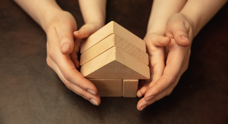 Vuxen och barns händer kring träblock som bildar ett hus