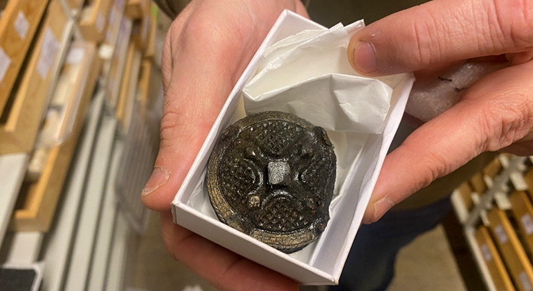Närbild av ett gammalt metallspänne som ligger i en ask.