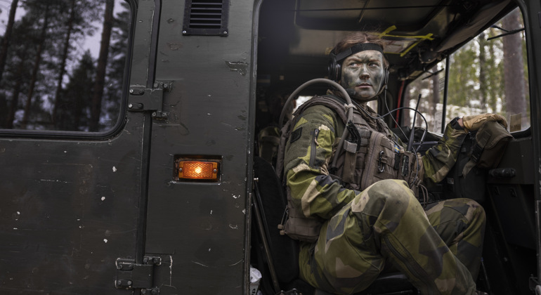 En kvinnlig plutonchef med kamouflagefärg i ansiktet sitter i en bandvagn med dörren öppen.