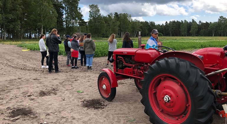 En åker med en röd traktor i förgrunden och en grupp människor intill.
