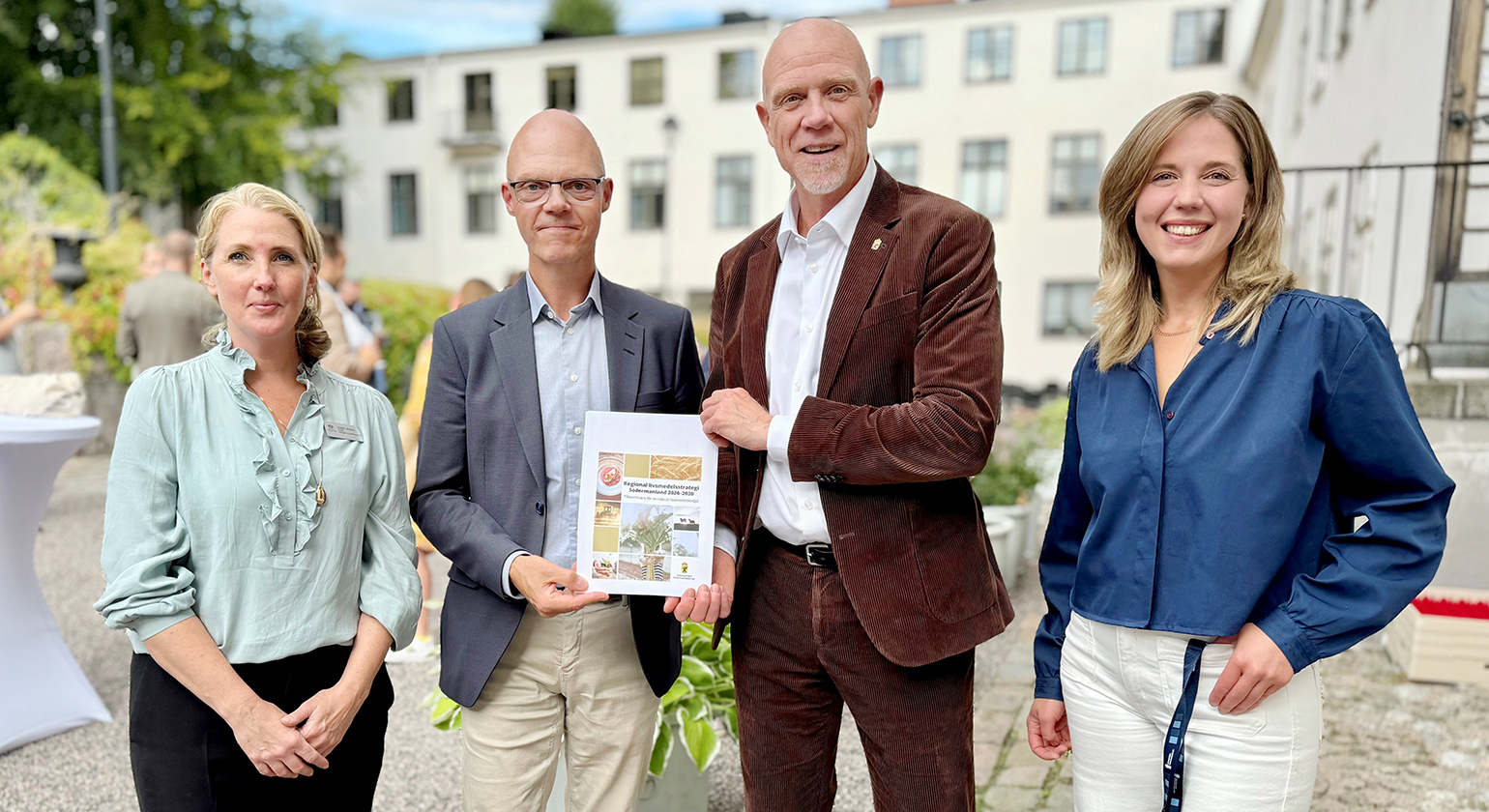 Två män håller gemensamt i den nya regionala livsmedelsstrategin, på varsin sida av dem står två kvinnor. I bakgrunden syns människor och residensets trädgård.