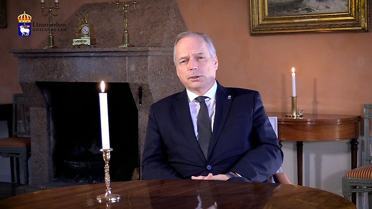 Landshövding Anders Flanking sitter vid ett bord med ett tänt stearinljus framför sig. I bakgrunden syns en öppen spis.