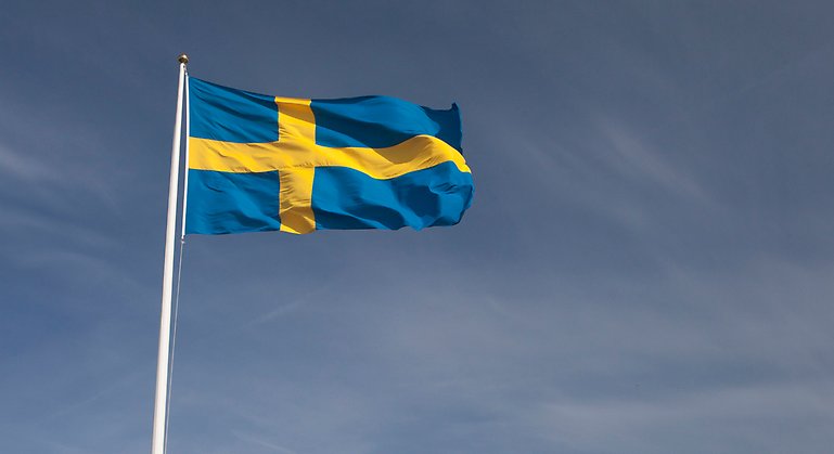 Svenska flaggan i blått med gult kors vajar med en blå himmel i bakgrunden.