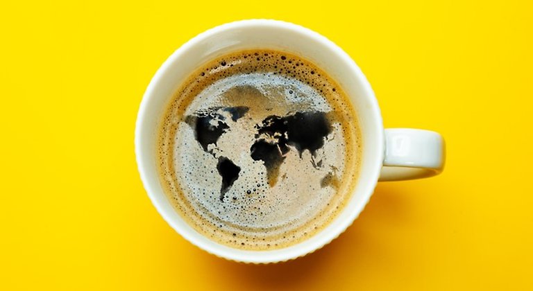 Foto på kaffekopp mot gul bakgrund där skum i kaffet bildar en världskarta