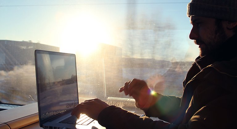 Man som sitter på ett tåg och jobbar vid sin dator