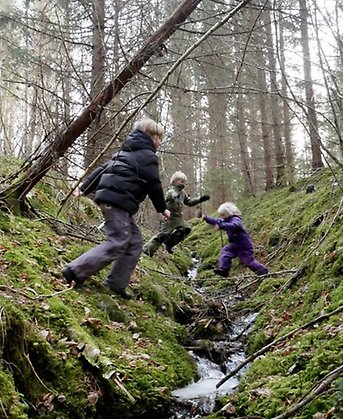 Tre barn hoppar över en torrlagd bäck i skogen