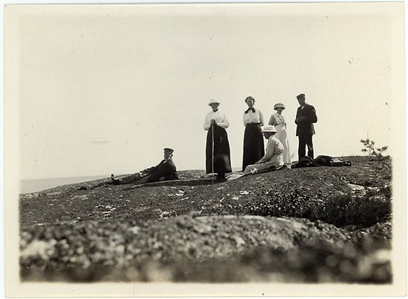 Gammalt blekt fotografi i svartvitt där några personer står och sitter på en klippa.