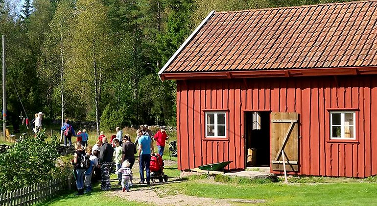 Ett rött trähus där människor passerar vid sidan sommarklädda.