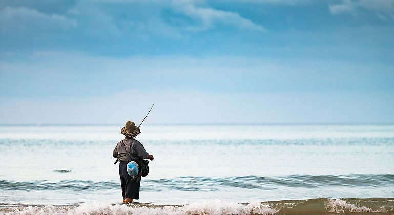 En kvinna står med ett fiskespö vid havet.