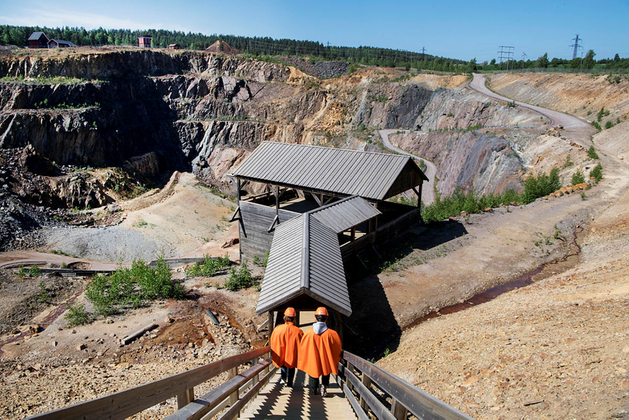 Två personer i orangea skyddskläder går ner för en trappa ner i Falu gruva. 