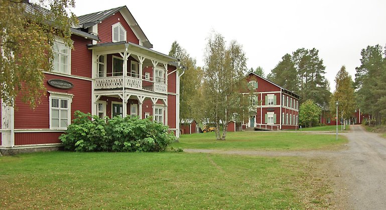 Tre stycken röda trähus med vita/gröna knutar och fönsterkarmar samt plåttak.