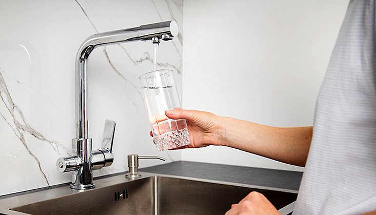 Person som fyller ett glas med vatten från en kökskran.