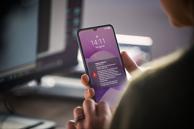Närbild på en hand som håller i en mobiltelefon med ett varningsmeddelande på skärmen.