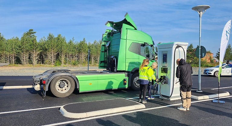 En lastbil står parkerad bredvid Jönköpings läns första snabbladdare för tunga fordon. Två personer står bredvid snabbladdaren och inviger den.