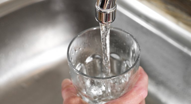 Hand som fyller ett vattenglas under en kran